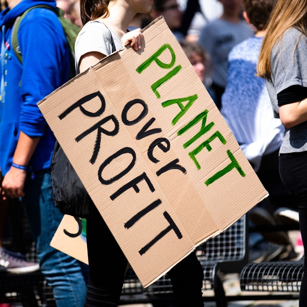 Ακτιβίστρια κρατάει πλακάτ που γράφει "ο πλανήτης πάνω από το κέρδος"