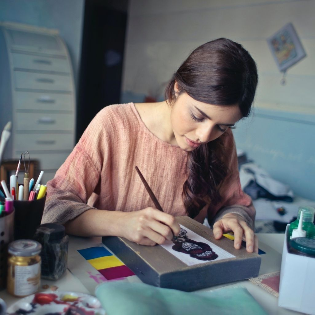Μία γυναίκα με καστανά μαλλιά ζωγραφίζει με νερομπογιές στο γραφείο της