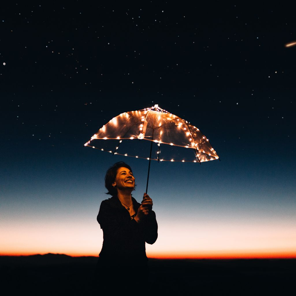 Γυναίκα κρατάει διάφανη ομπρέλα με λαμπιόνια και χαμογελάει