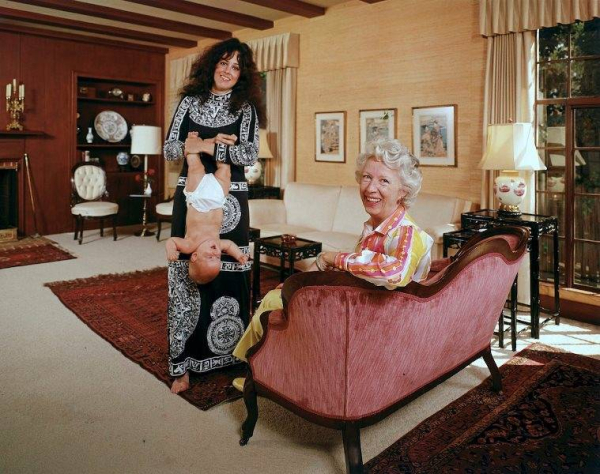 Singer Grace Slick of Jefferson Airplane holding her daughter  China  upside down by the ankles  Her mother  Mrs  Virginia Wing  sits on the sofa 