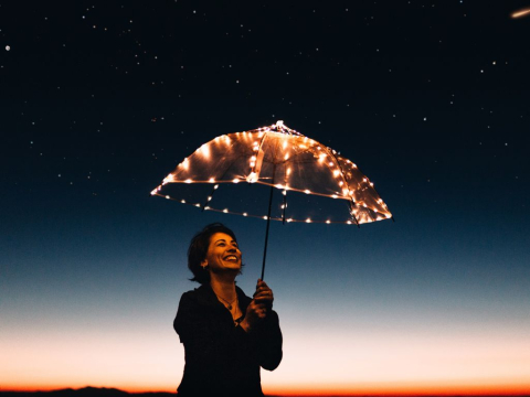 Γυναίκα κρατάει διάφανη ομπρέλα με λαμπιόνια και χαμογελάει