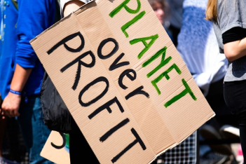Ακτιβίστρια κρατάει πλακάτ που γράφει "ο πλανήτης πάνω από το κέρδος"